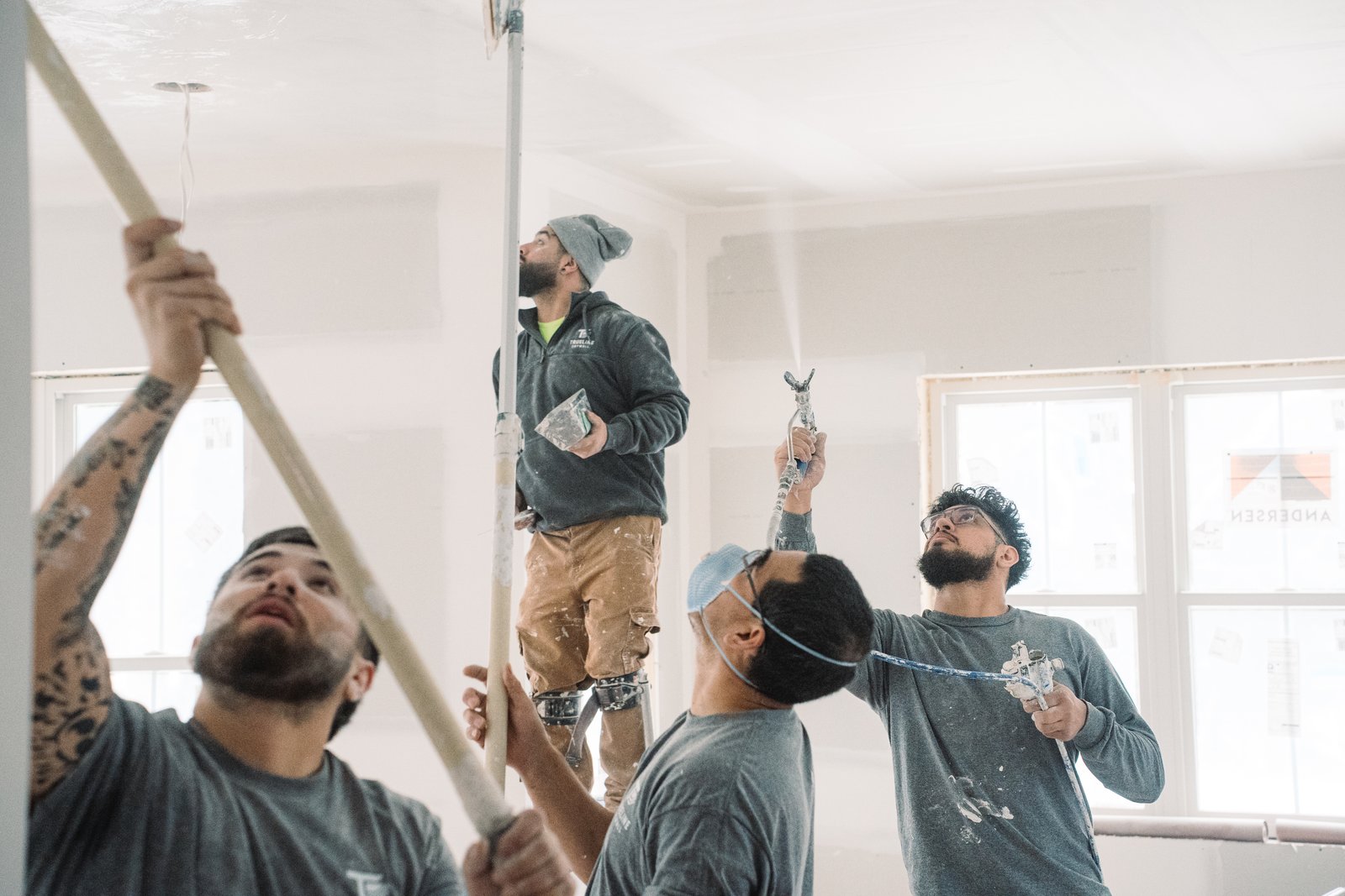 Construction workers installing drywall and framing in an unfinished interior room